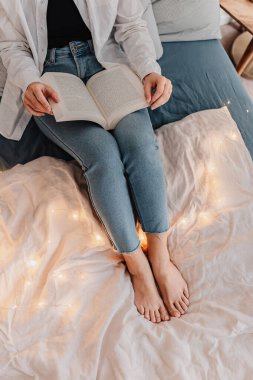 Sarı saçlı genç bir kadın yatakta kitap okuyor. Tarafsız renkler. Sıcak bir tatil günü. Dijital detoks. Hayatımız çevrimdışı, fişi çekiliyor. Kişisel tatminler. Sağlıklı ayrılık, birlikte yaşam. Yavaş yaşam.