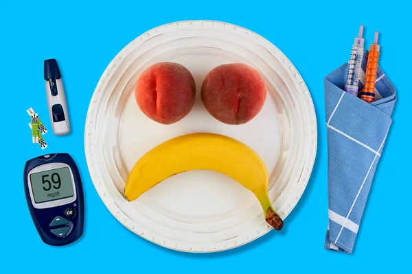 Plátano y melocotón en forma de emoticono sonriente triste en un plato blanco —  Fotos de Stock