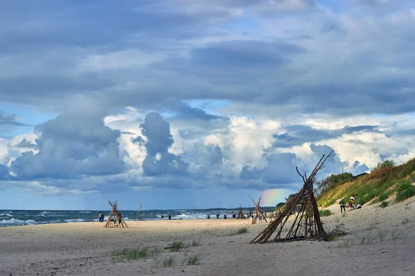 Piękne zachmurzone niebo z tęczą nad piaszczystą plażą z wigwamami — Zdjęcie stockowe