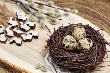 Quail eggs in a nest, wooden hares and pussy-willow branches with buds on a wooden board. Easter concept