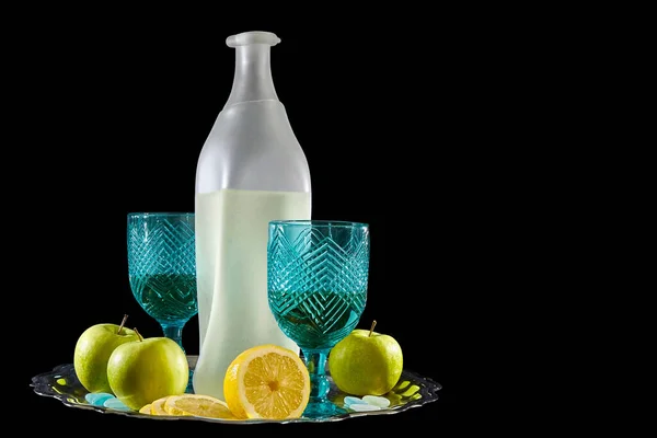 Bir şişe limonata ve bardakla dolu bir hayat. Etrafı elmalarla ve limonlarla çevrili. Arka plandaki metal tepside.
