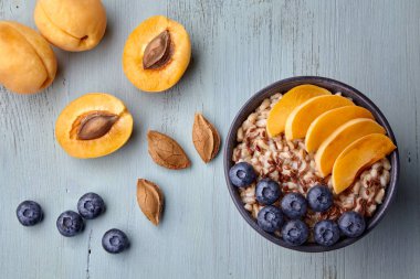 Whole grain oatmeal with apricot slices and blueberries on a painted wooden table. Vegan breakfast