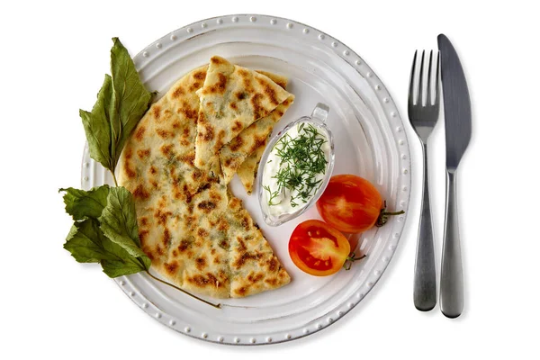Лепешки с сыром и травами и йогуртовым соусом на белой тарелке с столовыми приборами — стоковое фото