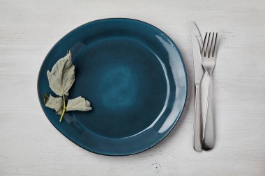 Zümrüt el yapımı seramik tabak ve beyaz ahşap bir masada çatal bıçak. Üst Görünüm Menüsü