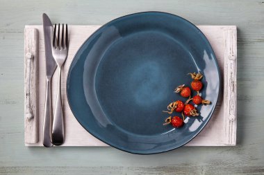 Beyaz ahşap tepside kurumuş gül kalçalarıyla süslenmiş el yapımı mavi seramik tabaklar. Menü. Üst görünüm