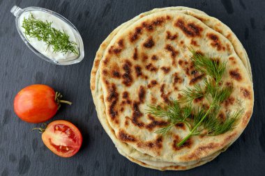Kızarmış tortilla peynirli, otlu ve yoğurt soslu siyah taş bir masada beyaz tabakta. Üst Manzara. Düz yatıyordu