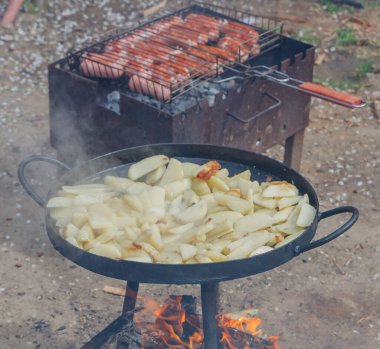 Çiğ patatesler et sosisleriyle ızgaranın yanında demir bir diskte kızartılır.