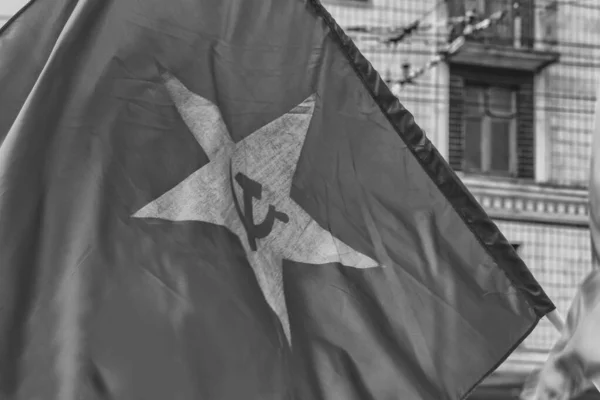 Soviet red waving flag with hammer and sickle on the background of the soviet building in black and white.
