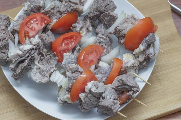  Doğranmış domatesli çiğ keçi eti ve tahta bir tahtanın üzerinde soğan.