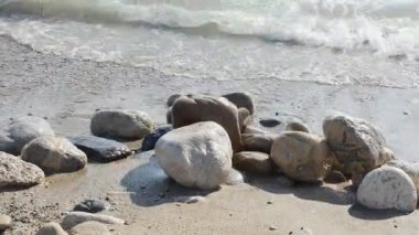 Yumuşak dalgaların hızlı, ritmik akışı kumlu ve çakıllı bir plajda yer alan pürüzsüz, güneşli kayaların üzerinde süzülüyor..