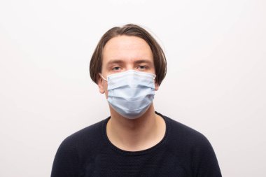 Yüzü maskeli bir adam beyaz arka planda kameraya bakıyor..