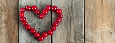 Ahşap bir arka planda kiraz rengi kalp şekli. Yıpranmış ahşap masada taze meyveler. Sosyal medya afişi veya başlığı.