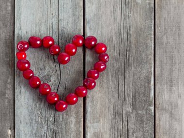 Ahşap bir arka planda kiraz rengi kalp şekli. Yıpranmış ahşap masada taze meyveler. Organik meyve hasadı .