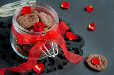 Çikolatalı kurabiye koyu ahşap bir masa ve bir kırmızı gül yaprakları üzerinde 