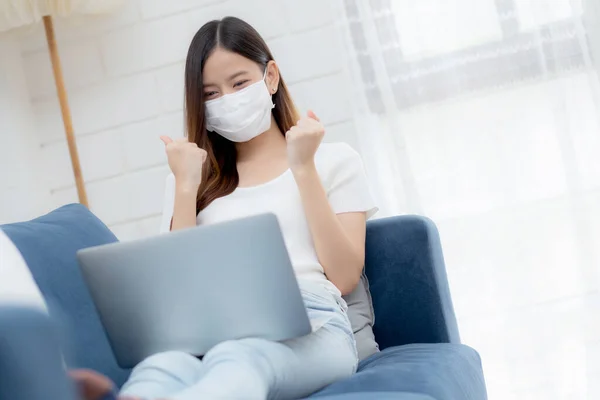 Young asian business woman in face mask work from home on laptop computer online to internet success in living room, girl in medical mask and quarantine for covid-19, stay home, new normal.