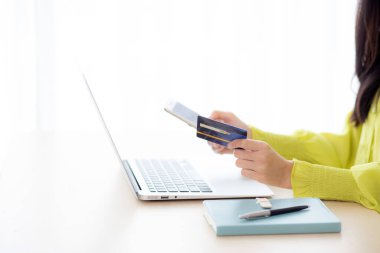 Yakın plan Asyalı genç iş kadını akıllı telefon kullanıyor ve kredi kartını tutarken online alışveriş ve ödemeyi evdeki dizüstü bilgisayarla yapıyor kadın banka kartı, iletişim konsepti.