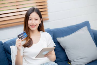 Asyalı genç bir kadın elinde tablet bilgisayar alımı ve ödemesiyle kredi kartı alışverişi yaparken gülümsüyor, bankamatik kartı alışverişi veya finans, yaşam tarzı ve e-ticaret konseptini kullanan bir kız..