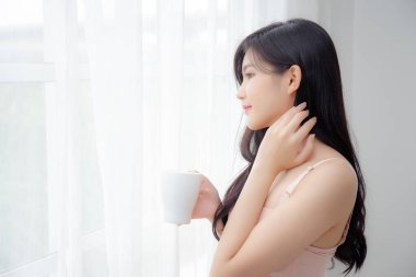 Sabahları iç çamaşırlı, güzel Asyalı seksi bir kadın pencerenin yanında kahve içiyor. Baştan çıkarıcı figürlü bir kız. Rahatlamak ve dinlenmek için içki içiyor..