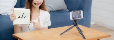 Genç Asyalı kadın evde e-öğrenim için öğrenciyle İngilizce öğretiyor, kız akıllı telefonlu sınıfta çalışıyor ve konuşuyor, evde kalıyor, yeni normal, eğitim kavramı.