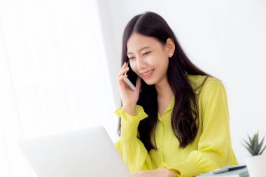 Genç Asyalı iş kadını ev ofisinde çalışıyor ve evde başarı için telefon ediyor, iş kadını masada dizüstü bilgisayar kullanıyor, iş yerinde konuşan kadın akıllı telefon, iletişim konsepti.