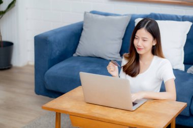 Genç Asyalı kadın internette dizüstü bilgisayarla internetten internet alışverişi yapıyor. Mutlu kız ödemesi kanepe, alışveriş ve ödeme, iş konsepti..