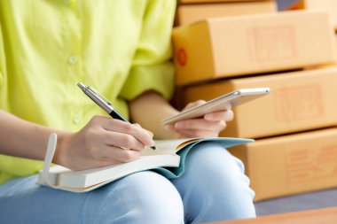 Girişimci görünümlü genç Asyalı kadın, internet üzerinden not defteri, çevrimiçi alışveriş, lojistik ve teslimat üzerinden müşteri sıralaması ve yazı sıralaması yapıyor, kadın ise kanepe ve iş KOBİ 'sinde çalışıyor..