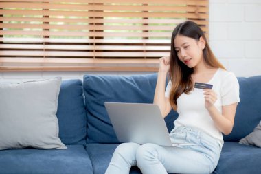 Genç Asyalı kadın internette dizüstü bilgisayarla internetten internet alışverişi yapıyor. Mutlu kız ödemesi kanepe, alışveriş ve ödeme, iş konsepti..