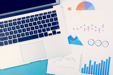 Dizüstü bilgisayar ve belgeler masa başında grafik ve çizelge ile istatistiksel finans, finans ve yatırım, dijital pazarlama ve gelir, iş ve iletişim kavramının büyümesi.