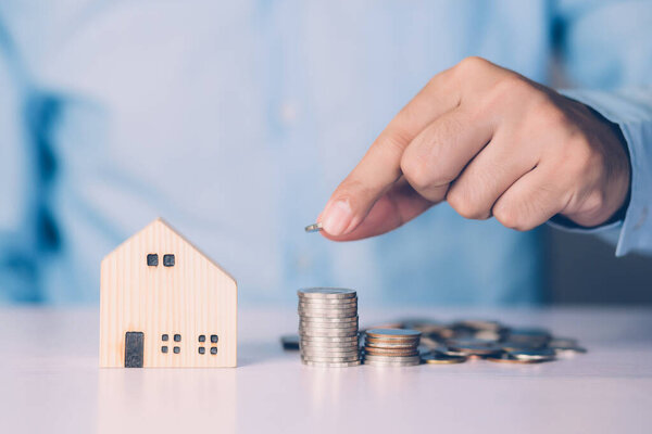 Hand of business man holding stack of coins and model home, wealth with finance and saving for residence and success, loan and mortgage for residential, investment for real estate, property concept.