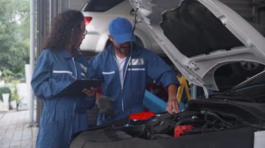 Tamirci ve üniformalı kadın tamirci garajda, tamirhanede, mühendis ve teknisyende, profesyonel, ulaşım ve araç konseptine sahip teşhis ve onarım için birlikte kontrol yapıyorlar..