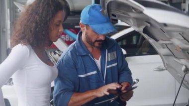 Elinde tablet tutan genç tamirci, müşteriye garajdaki sorun çıkaran araba motorundan bahsediyor ve anlatıyor. Teknisyen, tamir ve onarım için müşterisiyle aracın arızasını teşhis ediyor..