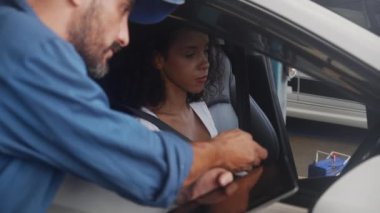 Elinde tablet tutan genç tamirci garajdaki sorun motorunu müşteriye anlatıyor ve anlatıyor. Tamir ve onarım için müşteri ile aracın teknisyen kontrolünde sorun var..