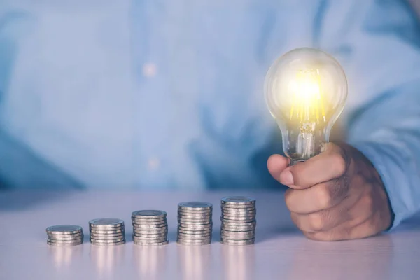 Hands of businessman holding light bulb while coin on desk, saving and finance for success, knowledge about deposit and earning and investment, solution and inspiration, business concept.