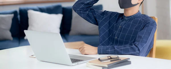 Young business man in face mask working from home with laptop computer and bored on desk for protection for outbreak of covid-19, male quarantine stay home using notebook with unhappy, new normal.