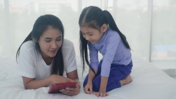 ベッドルームでベッドの上で学習や教育のために一緒にタブレットコンピュータを見て若いアジアの母親と小さな娘 家庭でインターネットにタブレットを見てお母さんと女の子 家族と技術の概念 — ストック動画