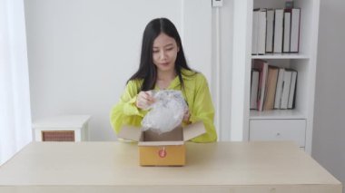 Genç Asyalı bir kadın paketleri online alışveriş ile açıyor evde tatmin olurken, bir kadın çevrimiçi mağaza alışverişi ile birlikte paketleri açıyor ve heyecanlı, dağıtım ve yaşam tarzı konseptiyle bakıyor..