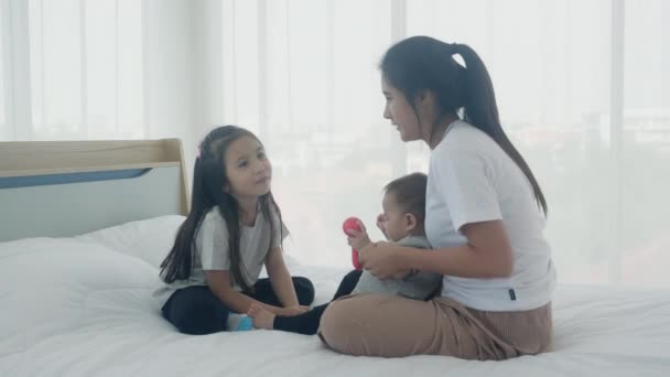 若いアジアの母親と娘が一緒にベッドの上で小さな赤ちゃんの女の子と遊んで座って お母さんと子供たちはリラックスし 感情と幸福と表現の家族 親と新生児 — ストック動画