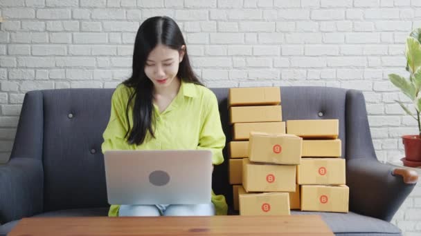 若いアジアの女性は オンラインショッピング ビジネス中小企業やスタートアップ 起業家や売り手とサービスの配信製品を購入する顧客の注文をチェックソファの上にラップトップコンピュータを使用して商人です — ストック動画