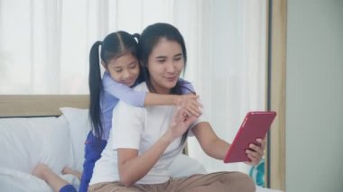 Genç Asyalı anne-kız video görüntüsü tablet bilgisayardan ailemizi selamlıyor, mutlu anne-kız ilişkisi olan iki kişi internetteki iletişim teknolojisini kullanıyor..