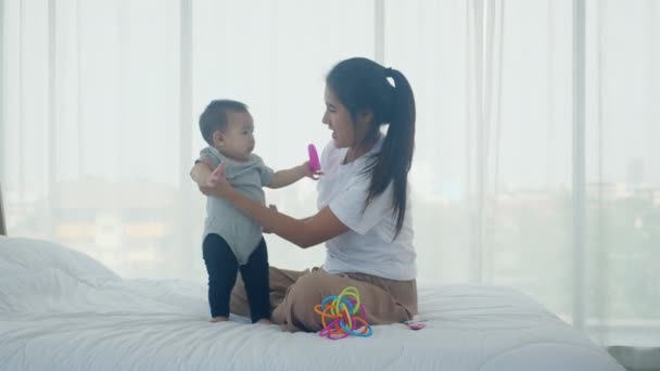 若いアジアの母親と赤ちゃんの女の子が一緒にベッドの上に座って遊んで お母さんと娘 幸せな 親と新生児のリラックスして肯定的な 感情と表現で感情と表現の家族 — ストック動画