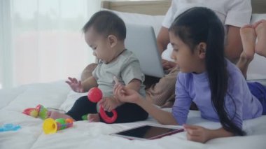 Genç Asyalı anne internette dizüstü bilgisayarla çalışıyor ve kız çocuğu yatak odasında tablet arıyor, iş kadını serbest çalışıyor ve çocuklar öğreniyor, yeni normal aile kavramı.