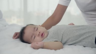 Genç Asyalı anne, küçük bir kızın yanağını öpüyor. Yatak odasında hassas bir şekilde yatıyor. Anne, yeni doğan ve özen gösteren bir anneyi, çocuklu bir ifadeyi, anne ve kızı, aile kavramını seviyor..