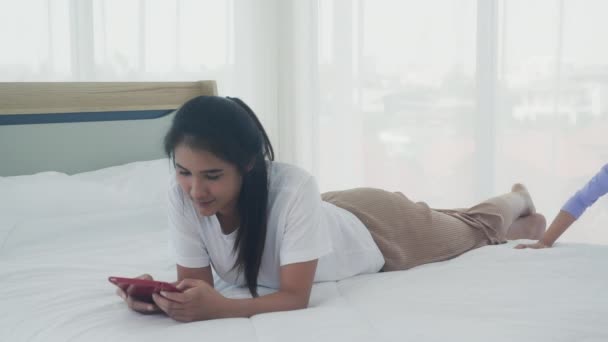ベッドルームで一緒にベッドの上でタブレットコンピュータを使用して若いアジアのお母さんと娘 オンラインに母と女の子のレジャー 関係と女性と子供 家族と教育の概念 — ストック動画