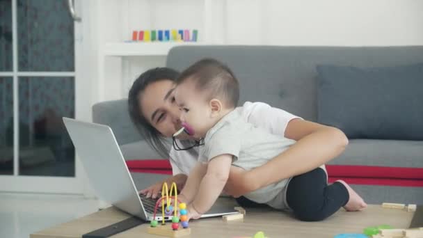 自宅のリビングで一緒に学ぶためにラップトップコンピュータを使用して幸せな若いアジアの母親と赤ちゃんの女の子 ノートブックの作業を使用して 彼女の新生児と母親 家族と教育の概念 — ストック動画