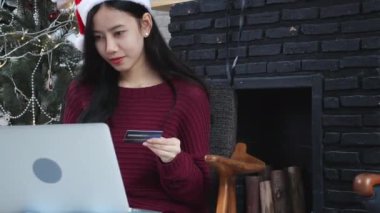 Genç Asyalı bir kadın Noel 'de online alışveriş yapıyor, dizüstü bilgisayarında kredi kartı, banka kartıyla kadın satın alma ve ödeme, tatilde xmas, mutlu yıllar, internetten alışveriş yapan müşteriler..