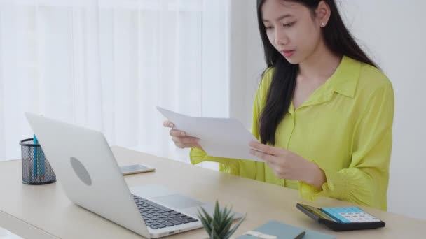 ノートパソコンで仕事をしている若いアジアのビジネス女性と 自宅のオフィスで紙の利益のためのグラフとレポートのグラフ 投資と収入を探しているビジネス女性 インフォグラフィックのデータ — ストック動画