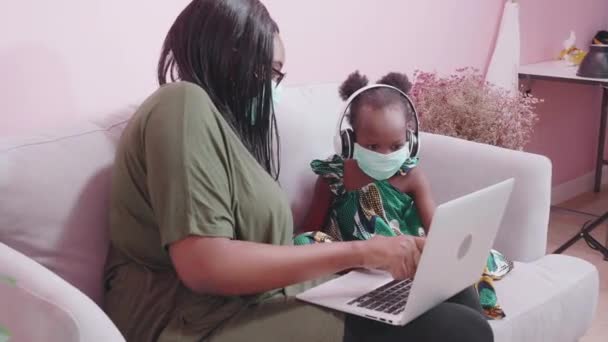 若いアフリカの母親と娘は音楽を聞いて 家でリラックスするために陽気で楽しい歌を歌います お母さんと小さな子供はラップトップコンピュータでEラーニングを勉強します 家族と教育の概念 — ストック動画