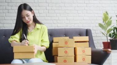 Genç Asyalı kadın paket kutusuna teslimat siparişi, nakliye ve lojistik, tüccar ve satıcı, işyeri sahibi veya KOBİ, çevrimiçi alışveriş ve e-ticaret için adres yazıyor..