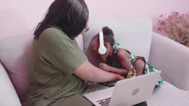 年轻的非洲母亲和女儿在家里用笔记本电脑学习和玩耍 小孩子带着耳机 带着疏远的教育理念进行电子学习 — 图库视频影像