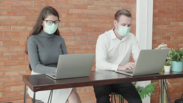 オフィスでラップトップコンピュータ上で働く顔マスクの若いアメリカのビジネスの男性と女性 社会的距離 新しい通常 ビジネスマンやビジネスの女性は パンデミックを保護するために距離を置いていますCovid — ストック動画